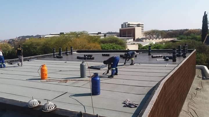 Team installing torch-on waterproofing membrane across a flat slab roof